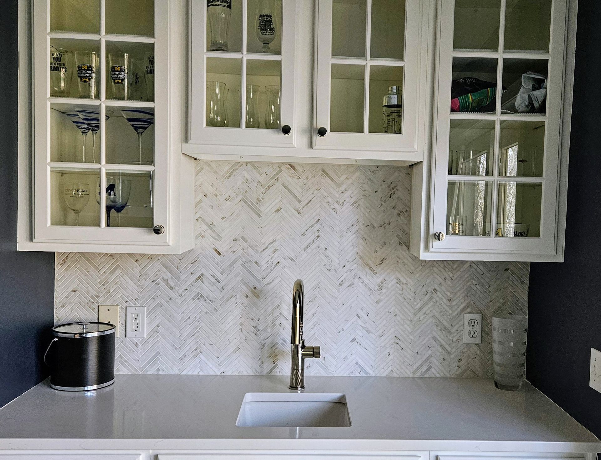 Kitchen with white cabinets, glass-front doors, and a backsplash. Sink with faucet in center.