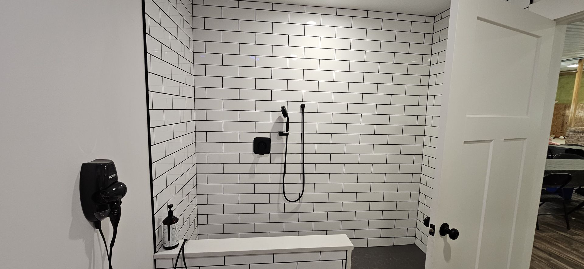 Bathroom with white brick tile walls, a showerhead, a white bench, and a white door.