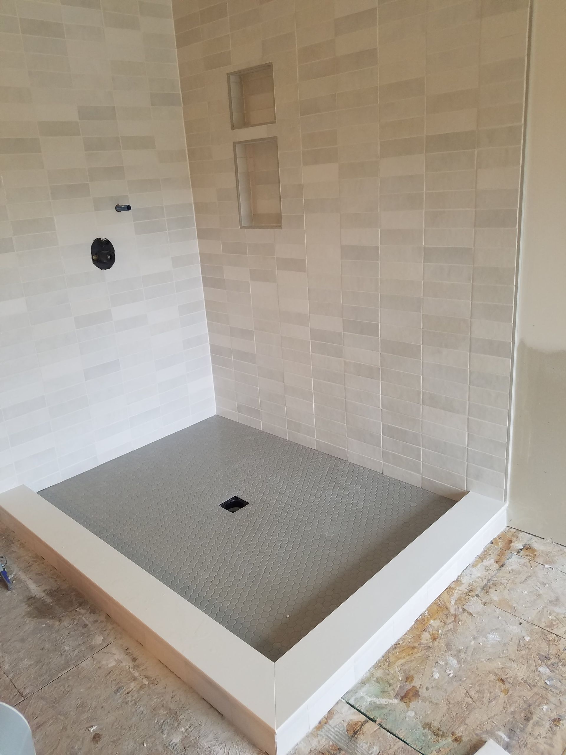 Tile shower in progress, with gray floor and white tile walls and trim.