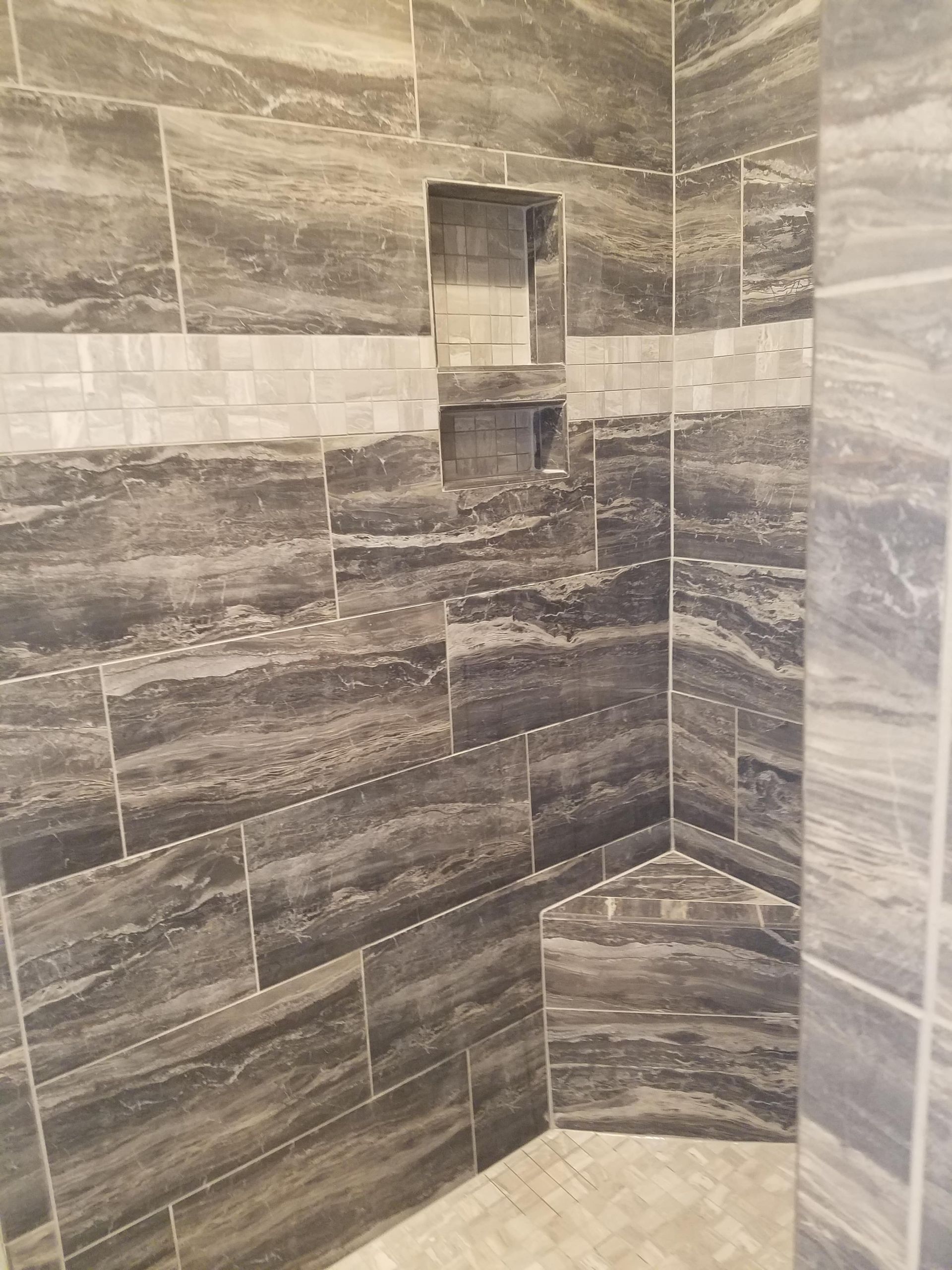 Tiled shower with a built-in niche and corner bench, featuring gray and white veined tiles.