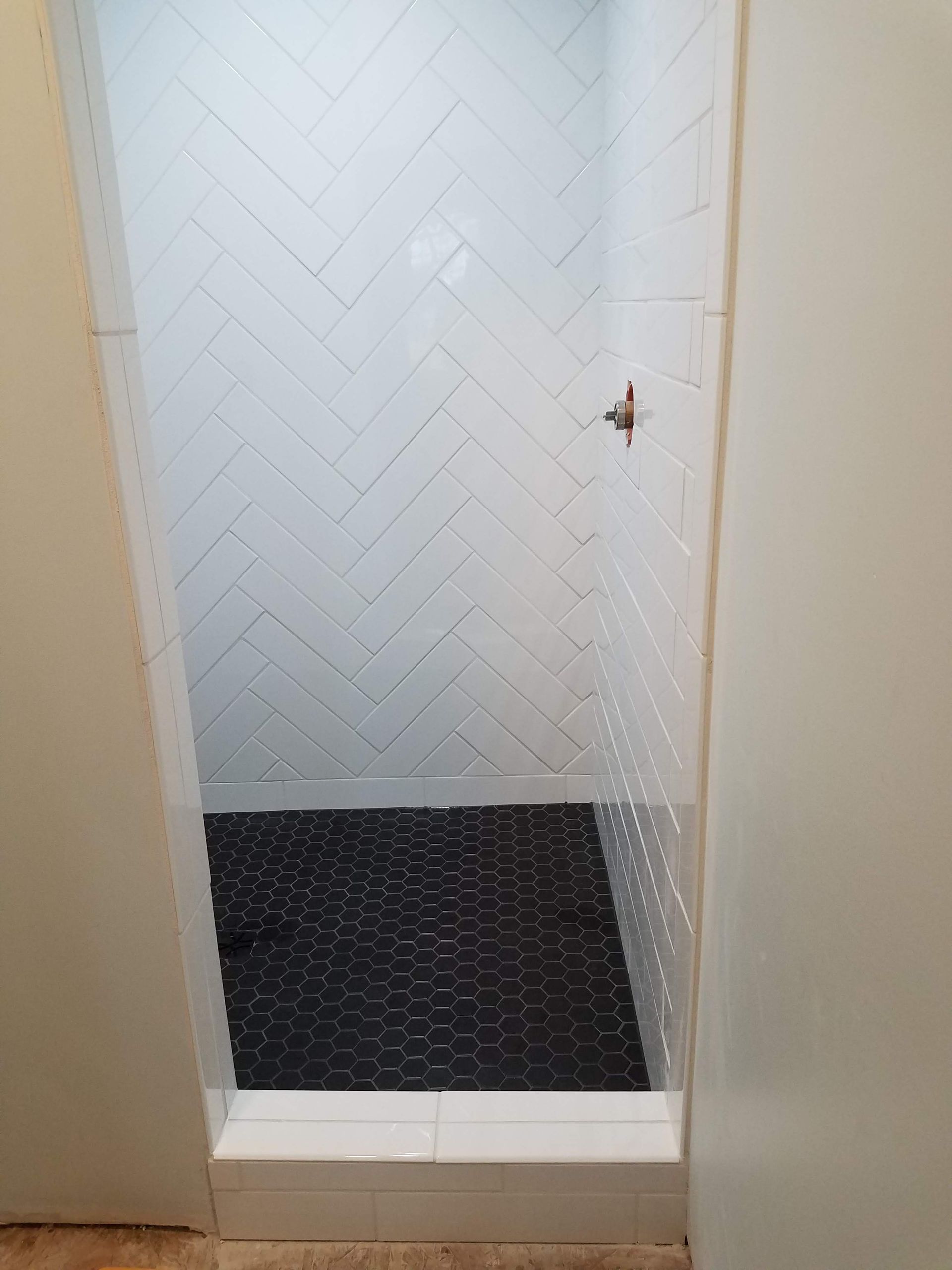 Shower stall with white herringbone tile walls, black pebble floor, and white trim.