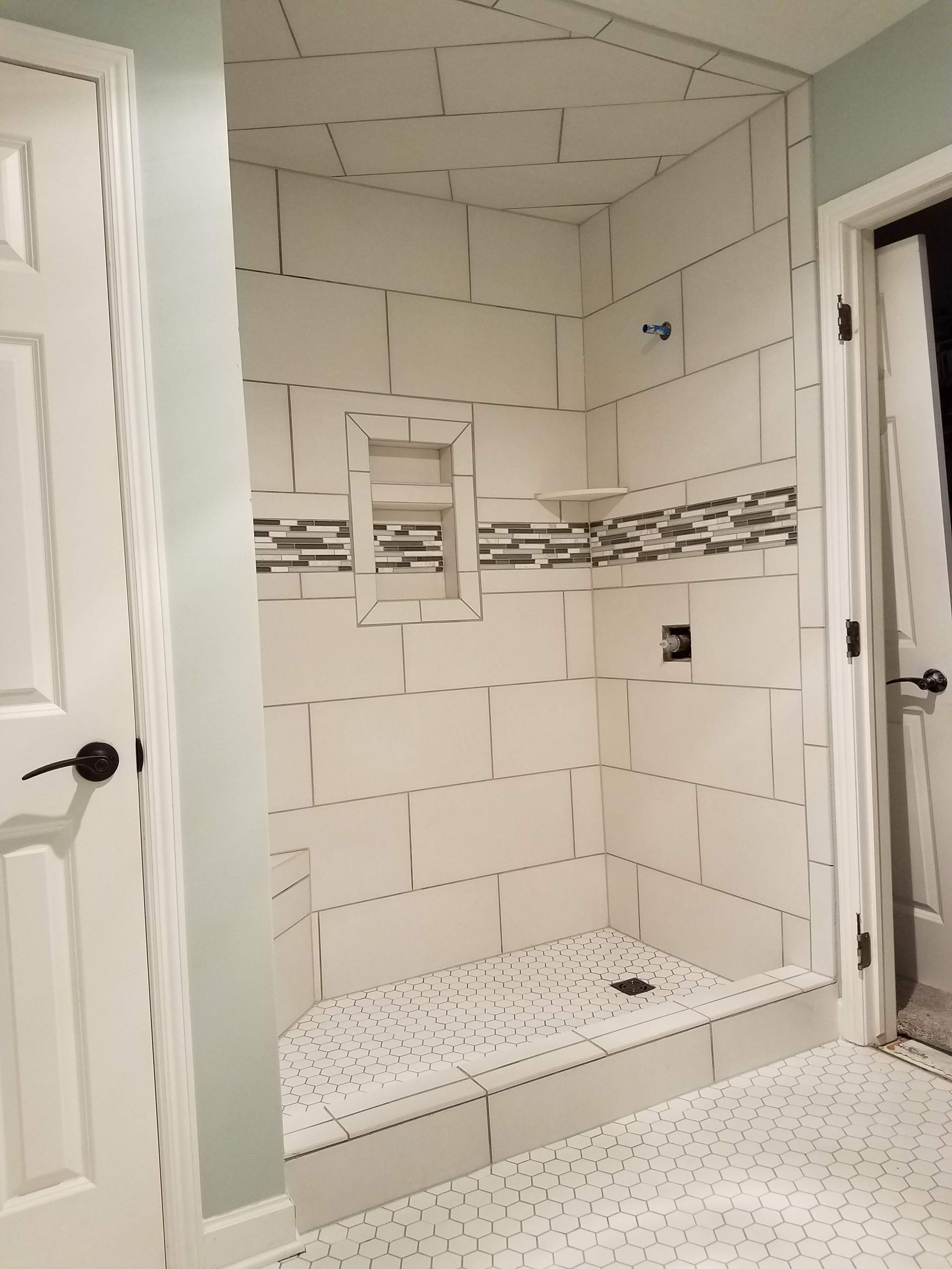 Newly tiled white shower with dark grout, mosaic accent, and corner shelf.