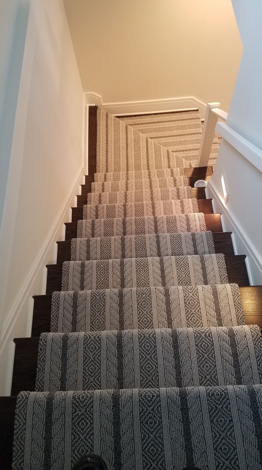 Staircase with patterned runner carpet and dark wooden steps, leading down from a white landing.