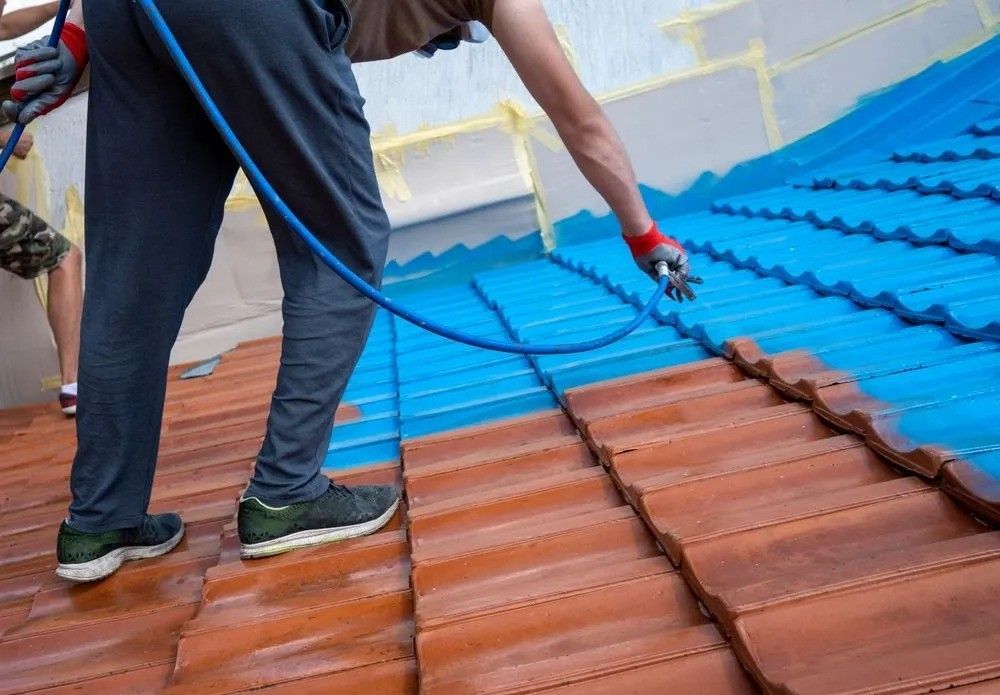 A Man Is Spraying Blue Paint On A Tiled Roof — Roofpoint In Kawungan, QLD