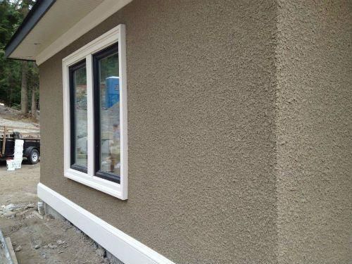Exterior wall with a stucco finish, window, and white trim.