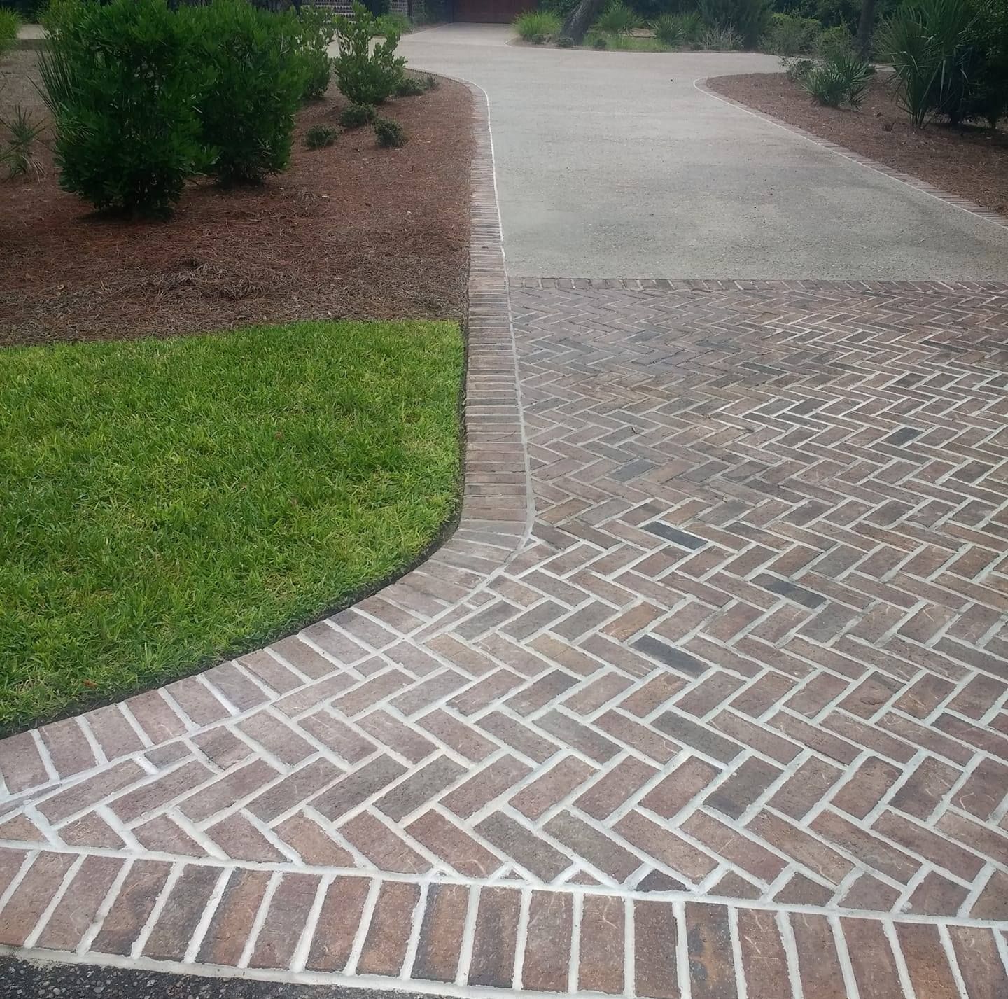 Brick driveway with grass and mulch border, concrete path.