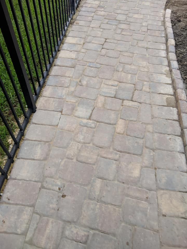 Brick walkway with black railing on the left and a curved border on the right.