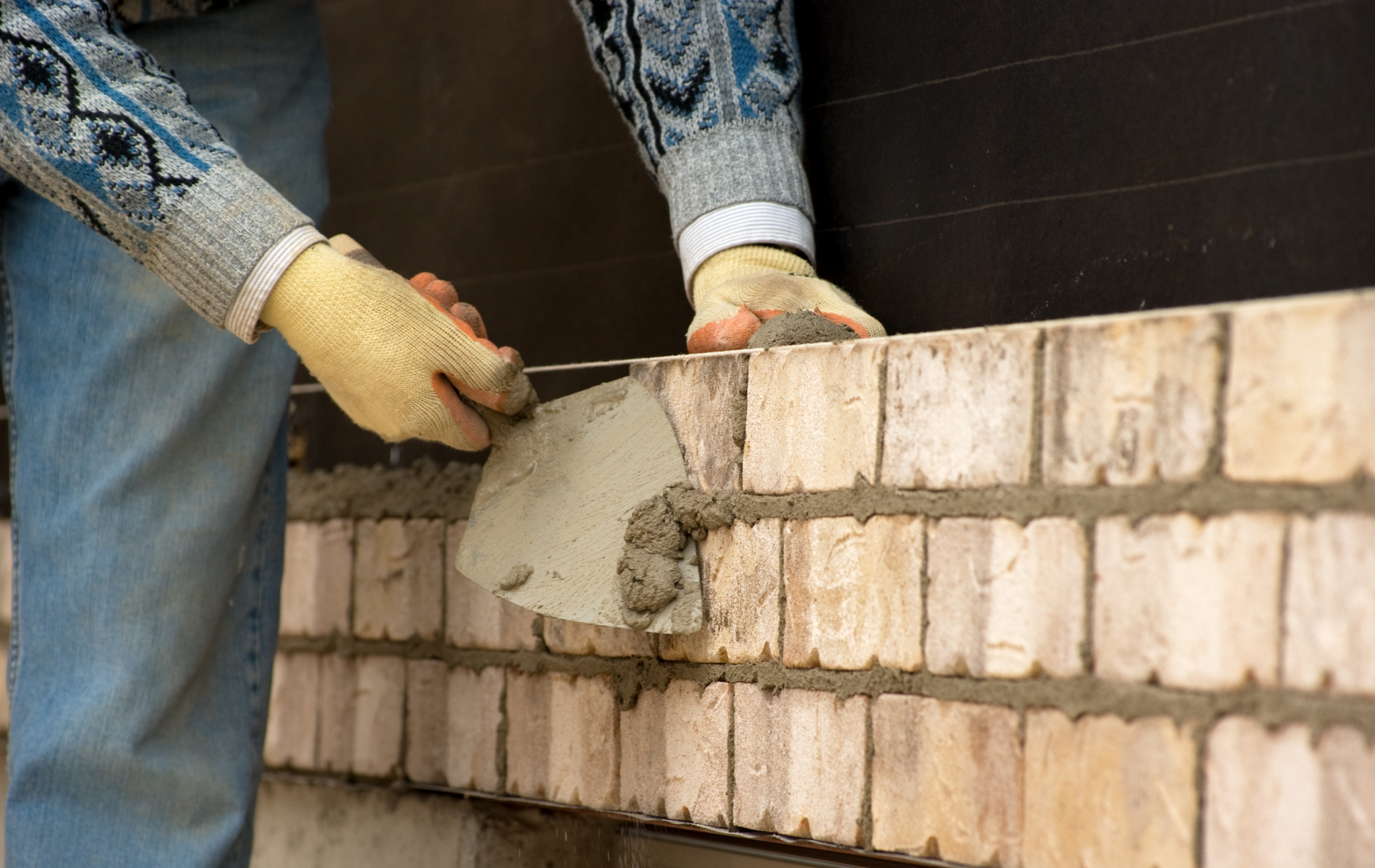 Bricklayer using a trowel to apply mortar on a brick wall.