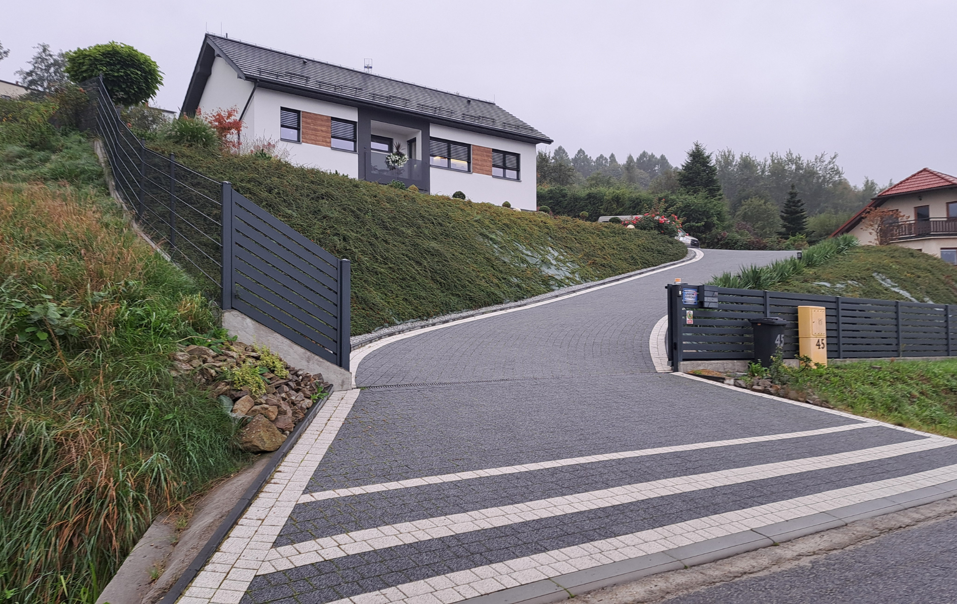 A house on a hillside with a dark paved driveway and gray fence.