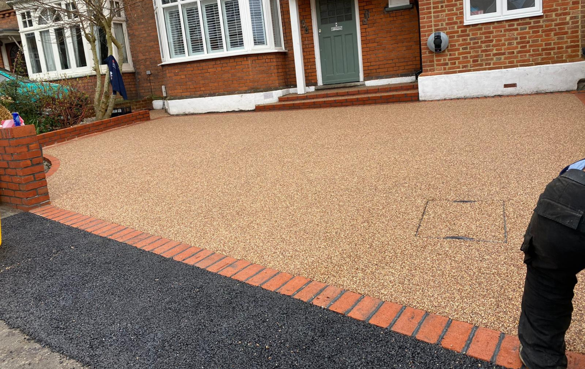 Gravel driveway with brick edging in front of a house; a person in work clothes is in the right corner.