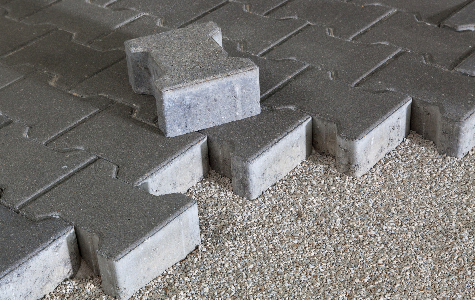 Gray interlocking pavers being installed on a bed of small gravel.
