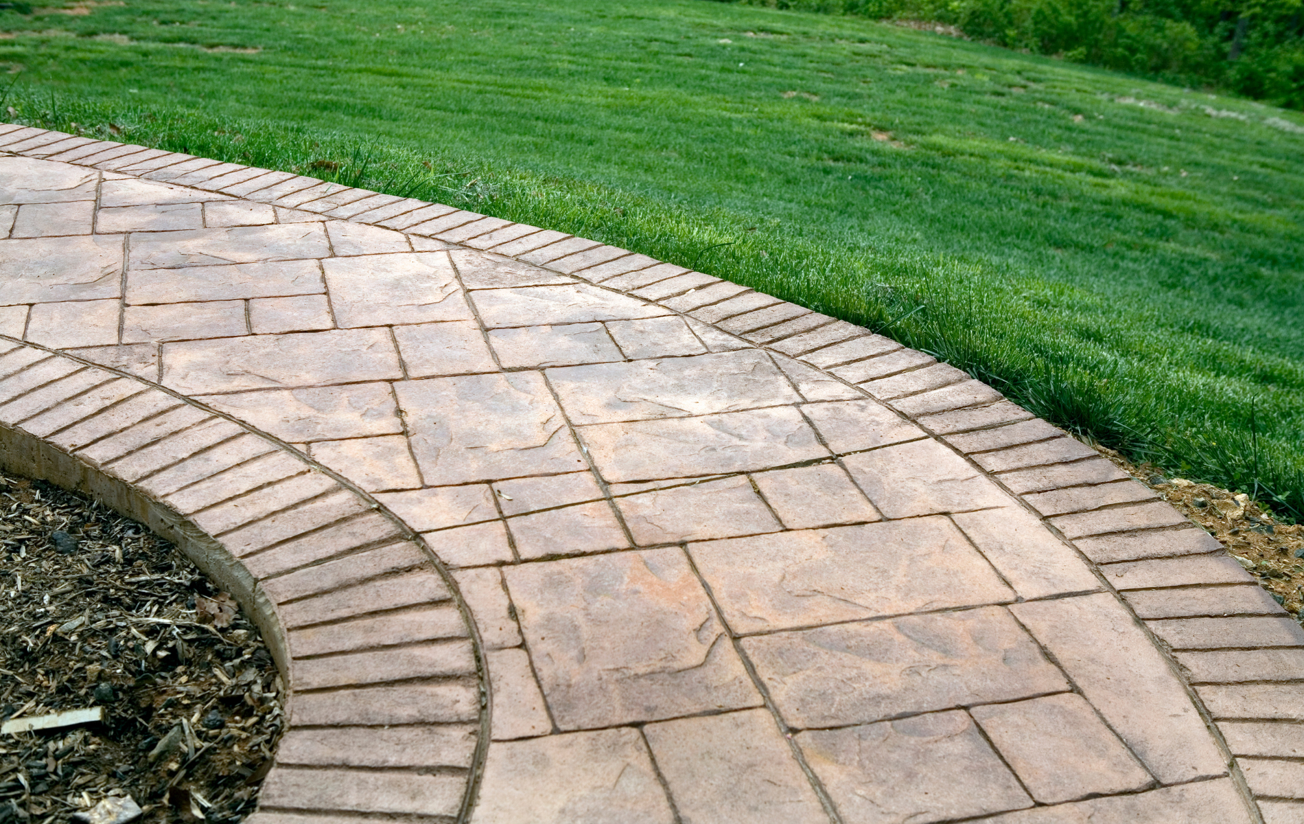 Stone walkway curving through green grass. Brown paving stones with brick edging.