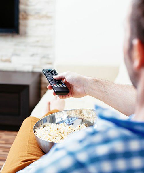 Man Changing Channel on TV and Eating Popcorn — Coastwide Antennas in Wamberal NSW