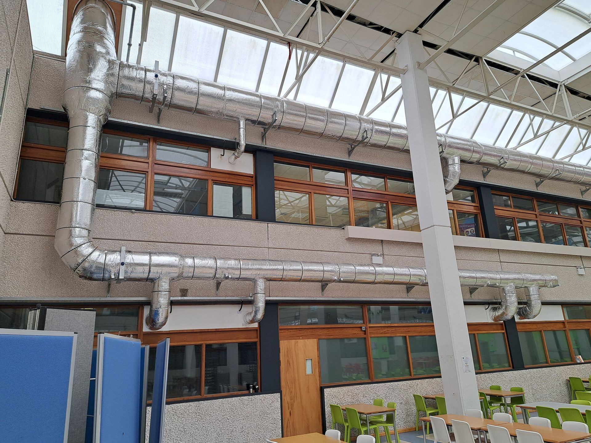 Interior view of a building with air ducts near a windowed wall and dining tables.