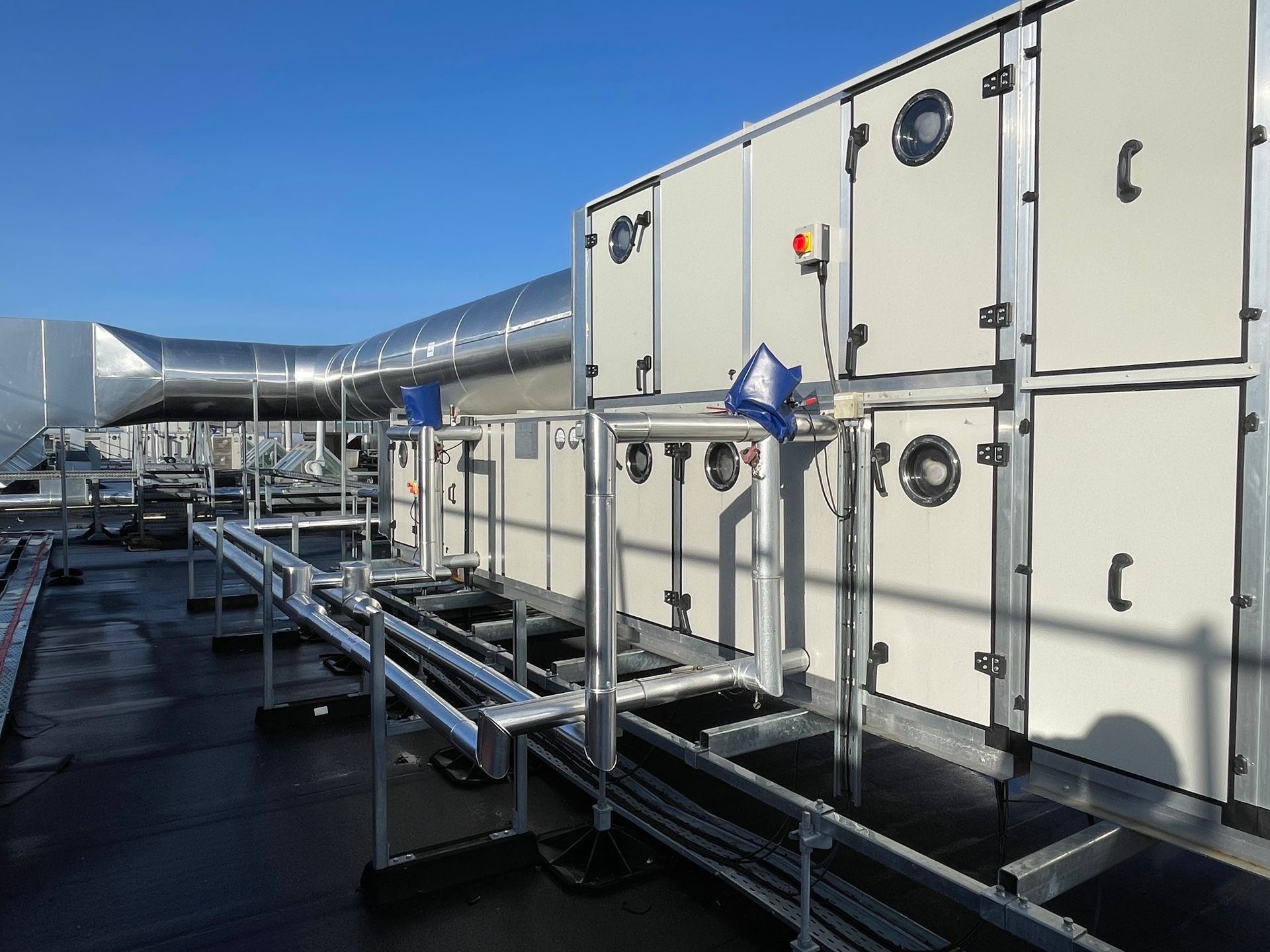 HVAC rooftop equipment; large rectangular units, ductwork, metal support structures, on a flat roof under a blue sky.