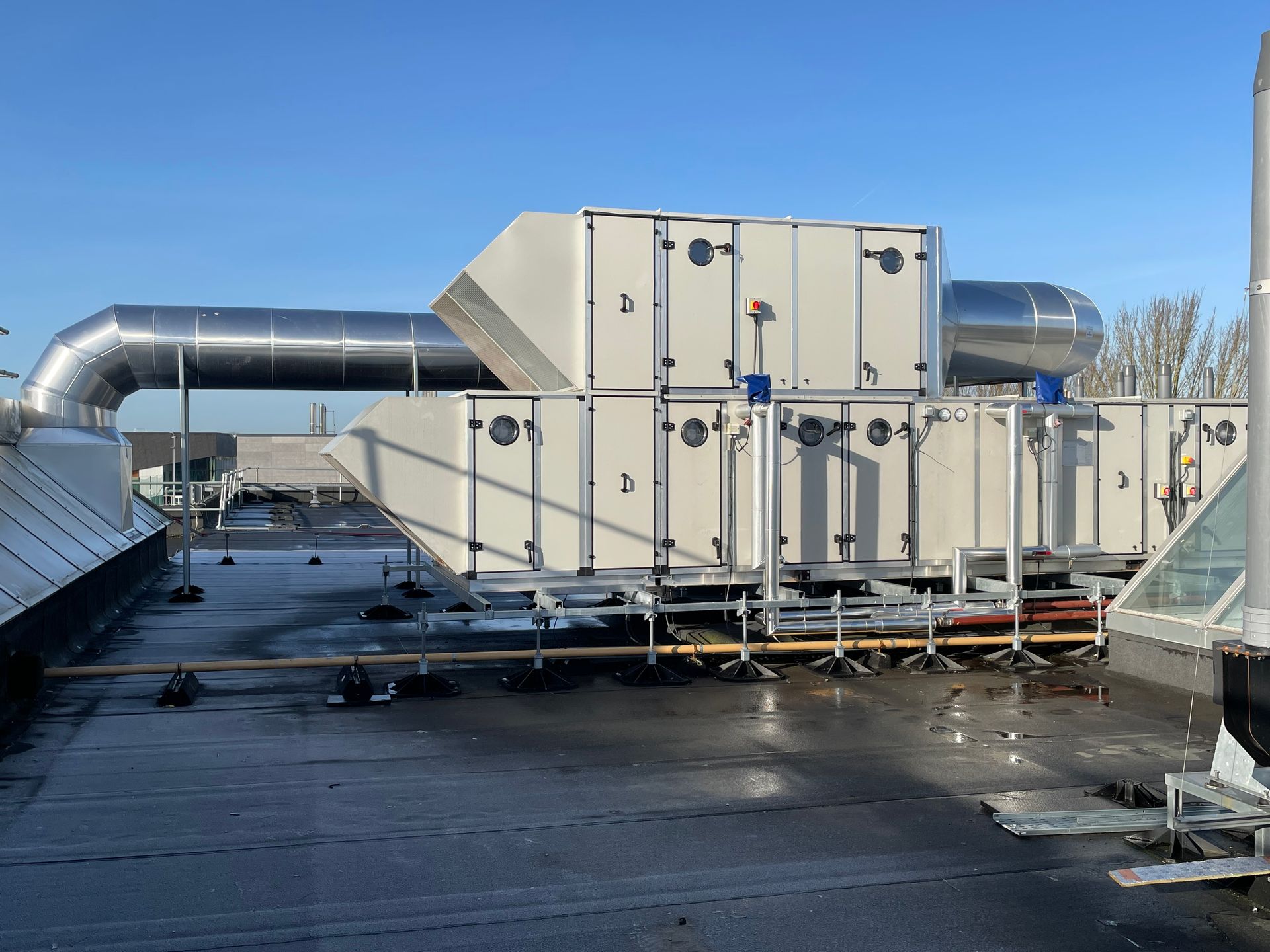 HVAC rooftop unit, silver ducts, light gray rectangular enclosures, mounted on a flat roof under a blue sky.