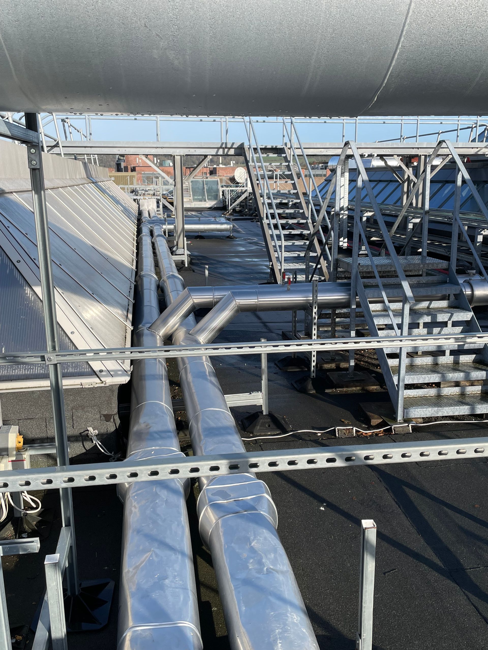 Metal pipes and scaffolding on a rooftop with stairs, a sunny day.