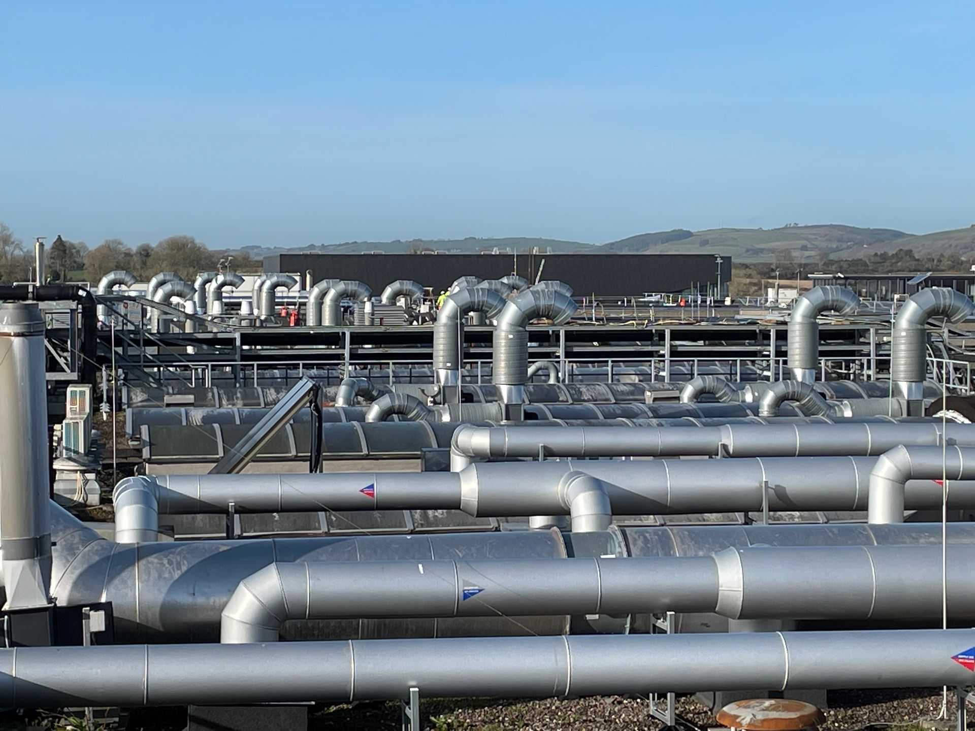 Silver industrial pipes and machinery in an outdoor setting, likely a plant.