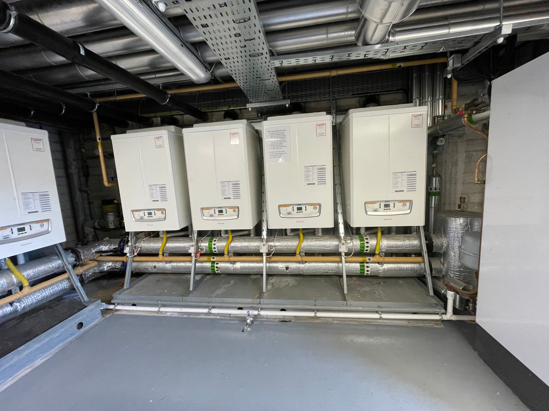 Four white boilers lined up in a utility room, with pipes and wiring visible.
