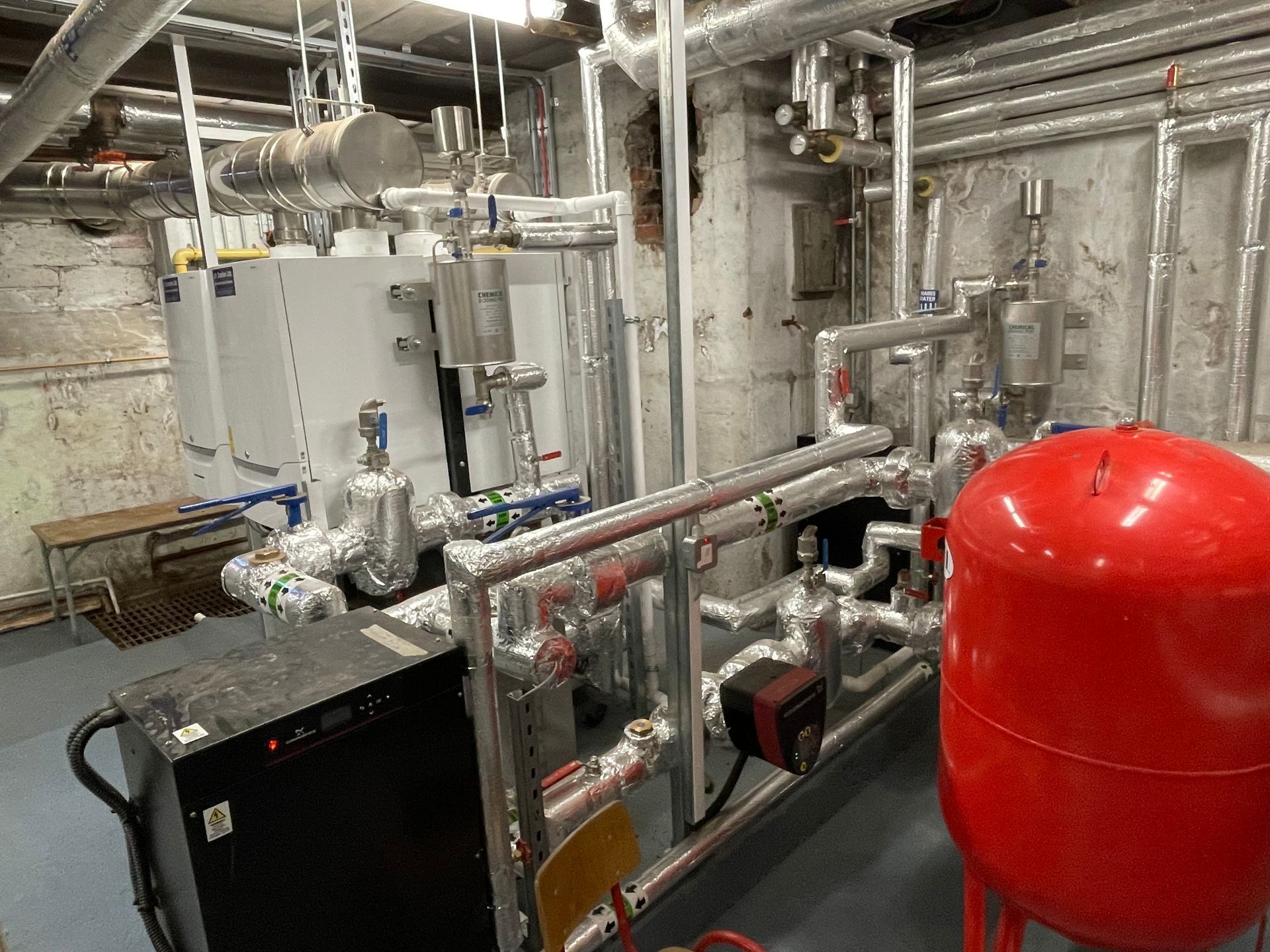 Industrial room with heating system components, pipes, and a red tank.