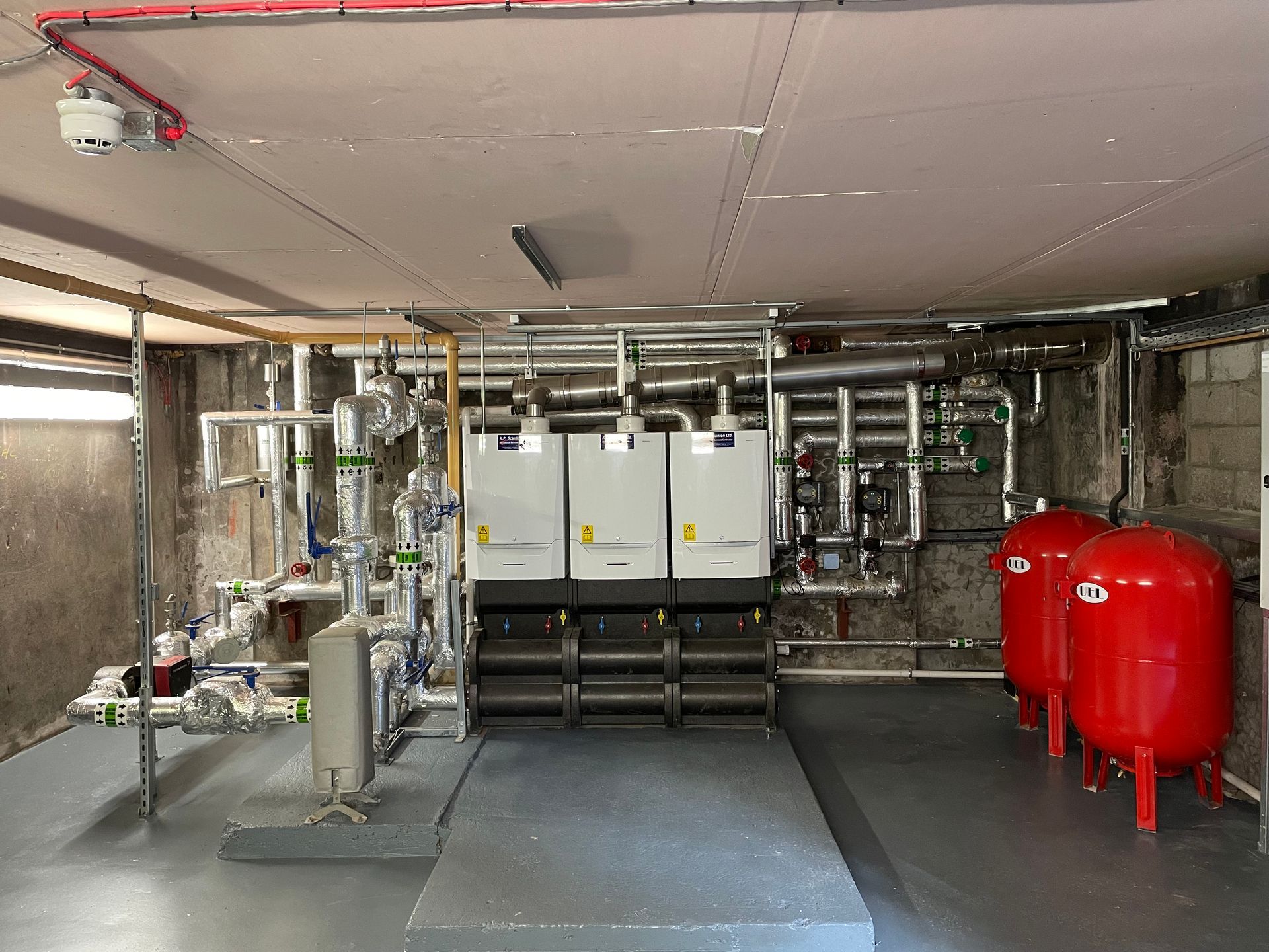 Boiler room with three white boilers, red tanks, and pipes.