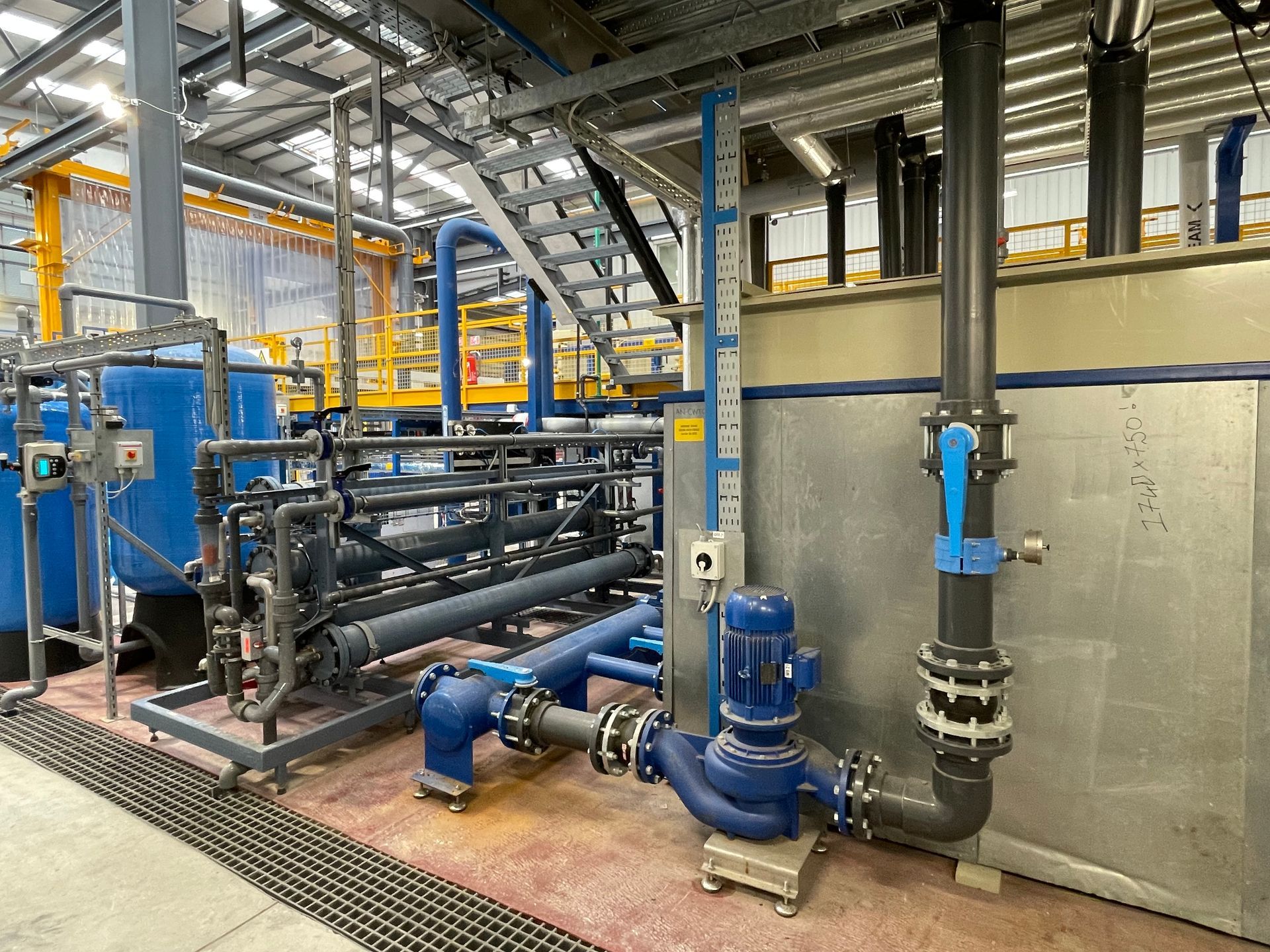 Industrial water treatment system with blue pipes, tanks, and pump in a factory setting.