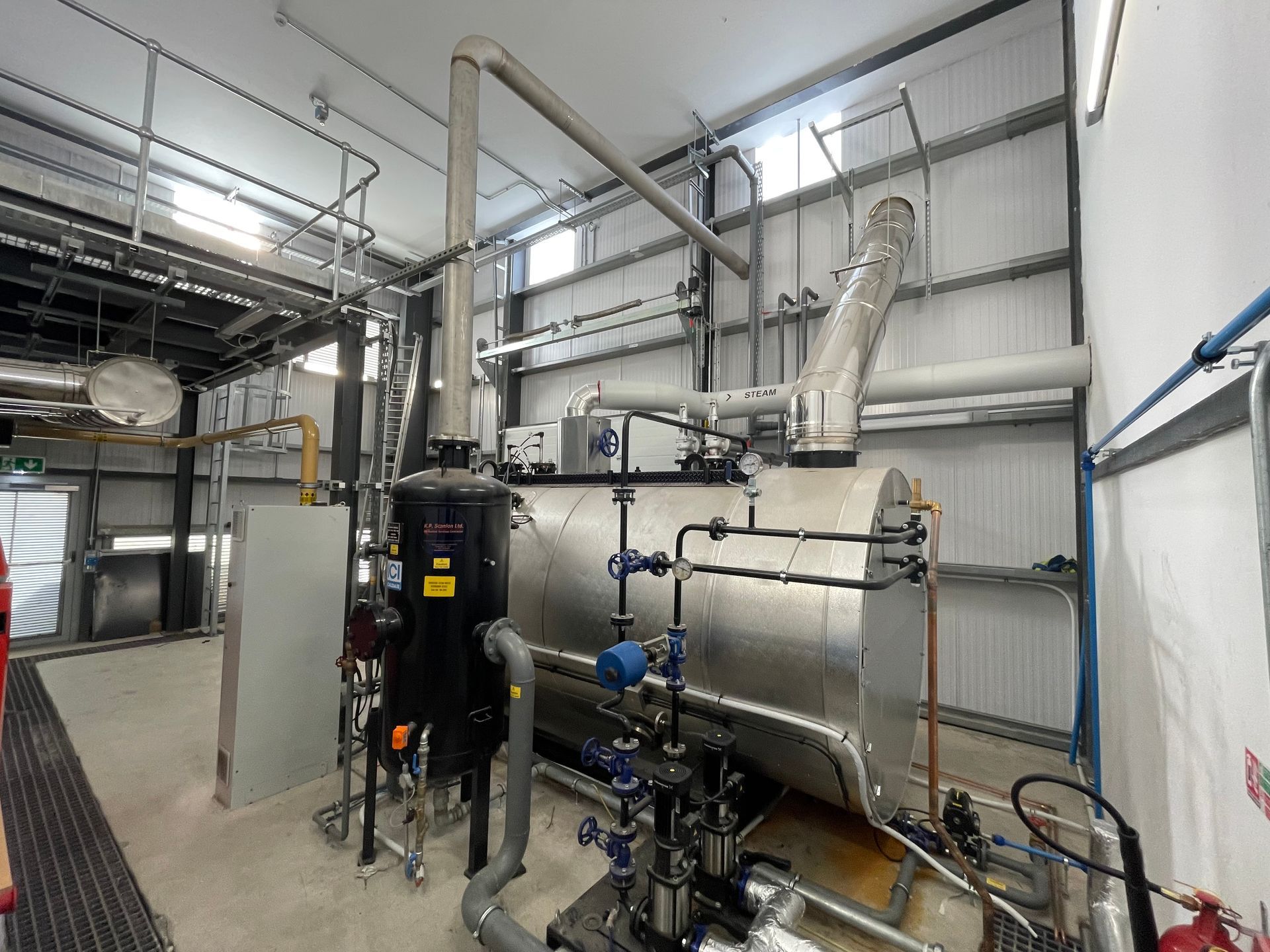 Industrial machinery within a building. Silver tank, black filter, pipes, and metal framework.