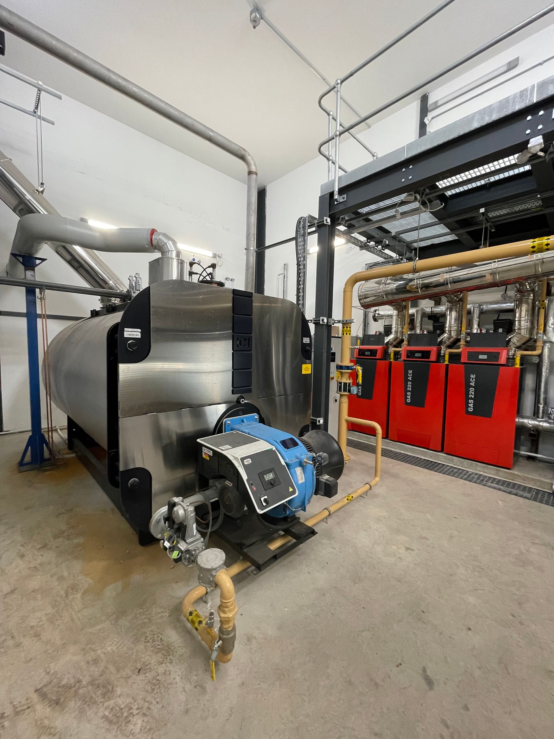 A large industrial boiler with blue burner and connected pipes in an equipment room.