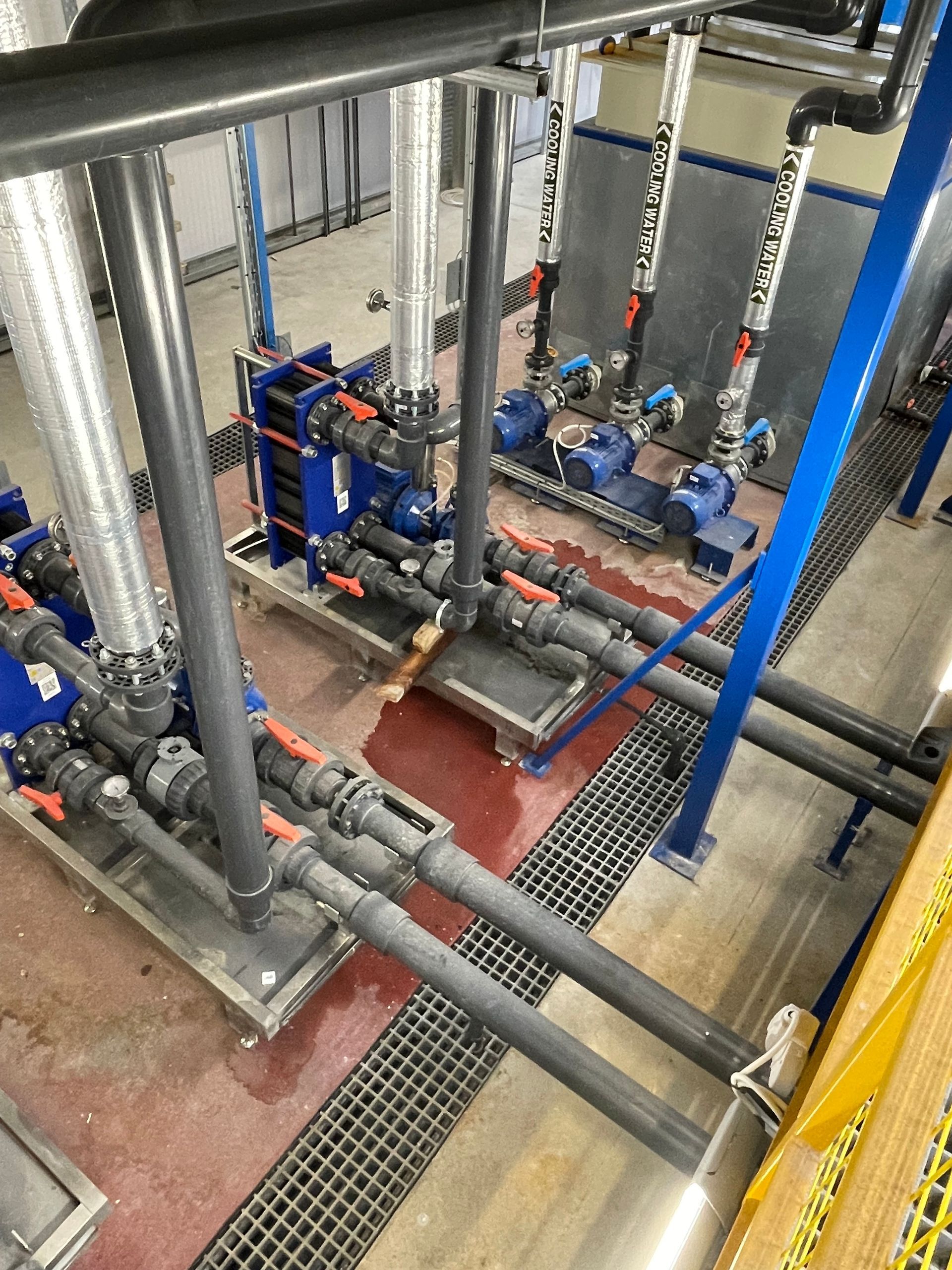 Industrial piping and pumps with valves, set indoors, blue, gray, and silver.