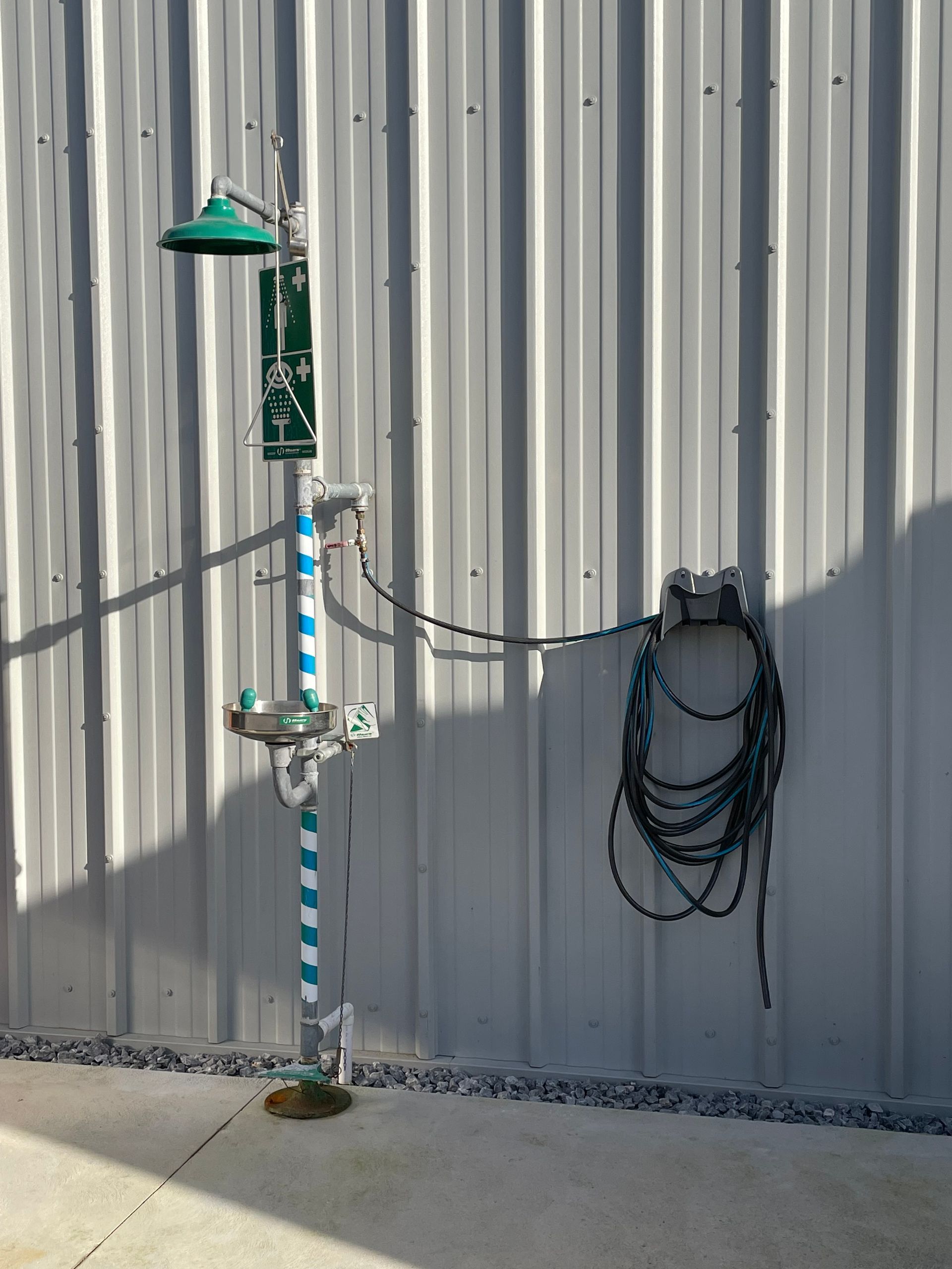 Emergency safety shower and eyewash station mounted on a corrugated metal wall.