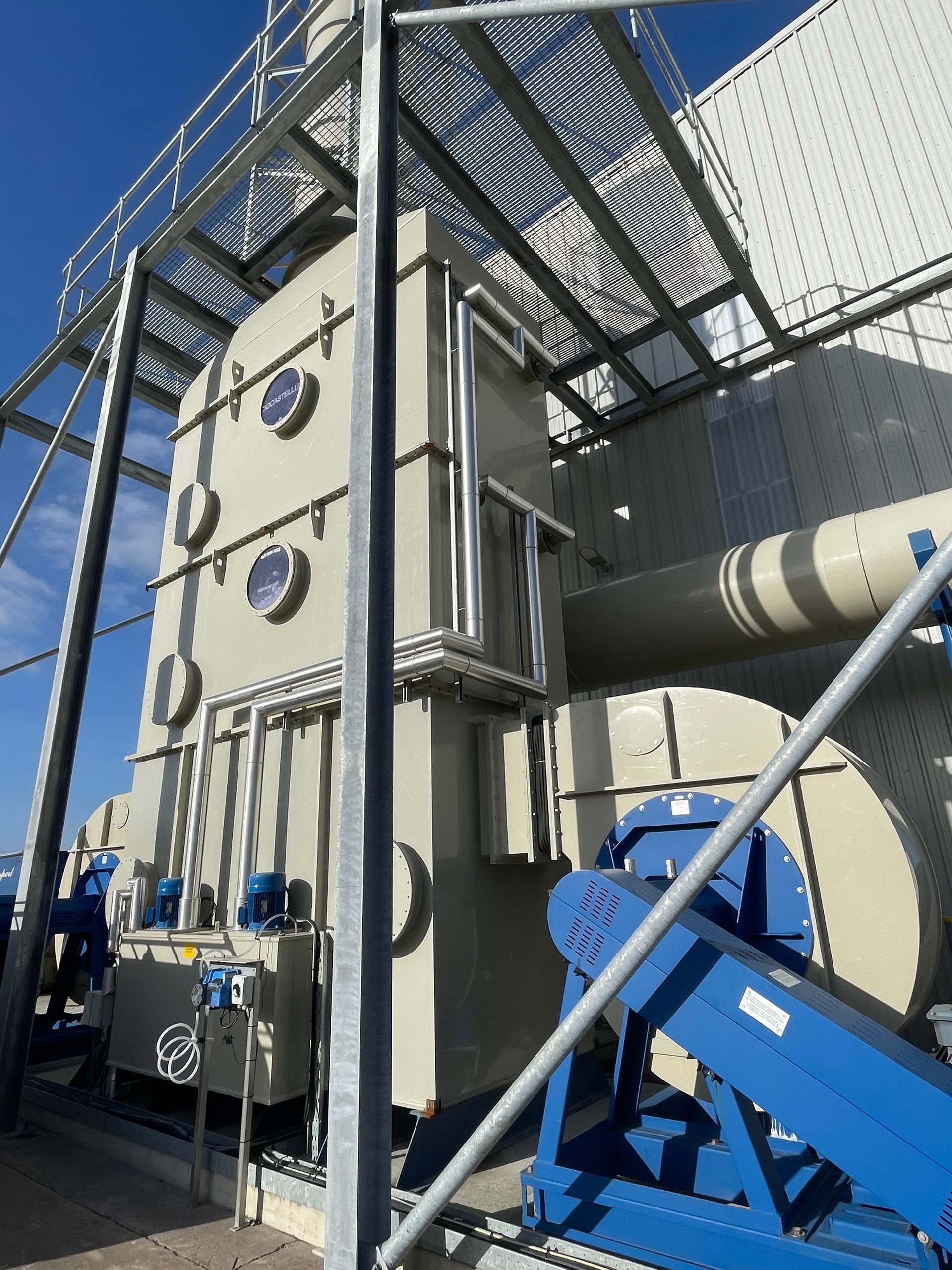 Industrial equipment, tan with blue accents, outdoors. Metal framework and ventilation components.
