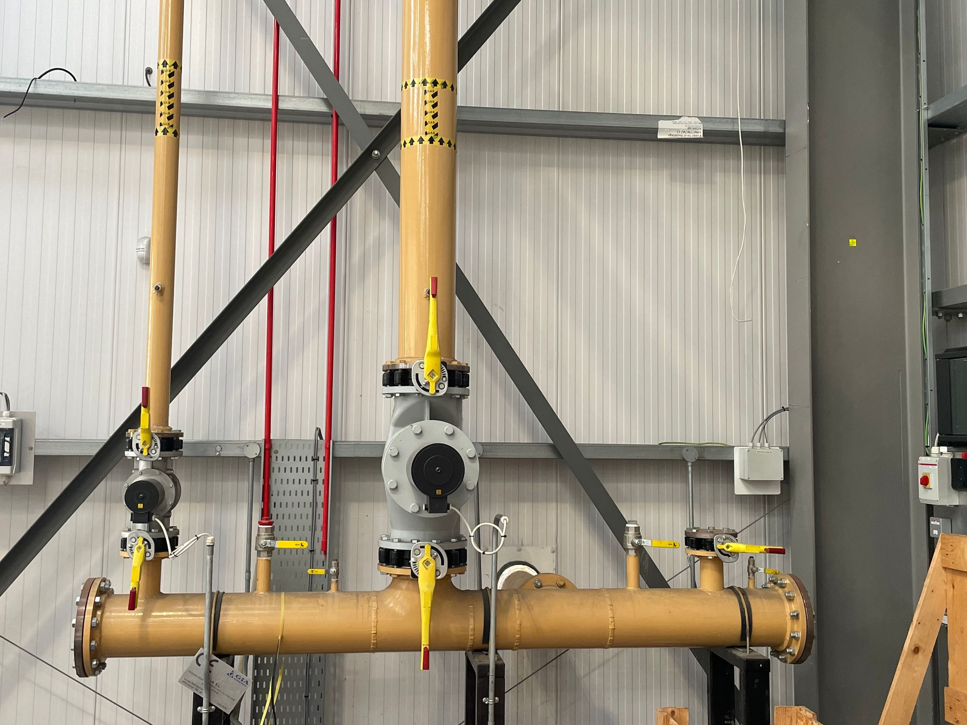 Brown industrial pipes with valves, against a metal wall with support beams.