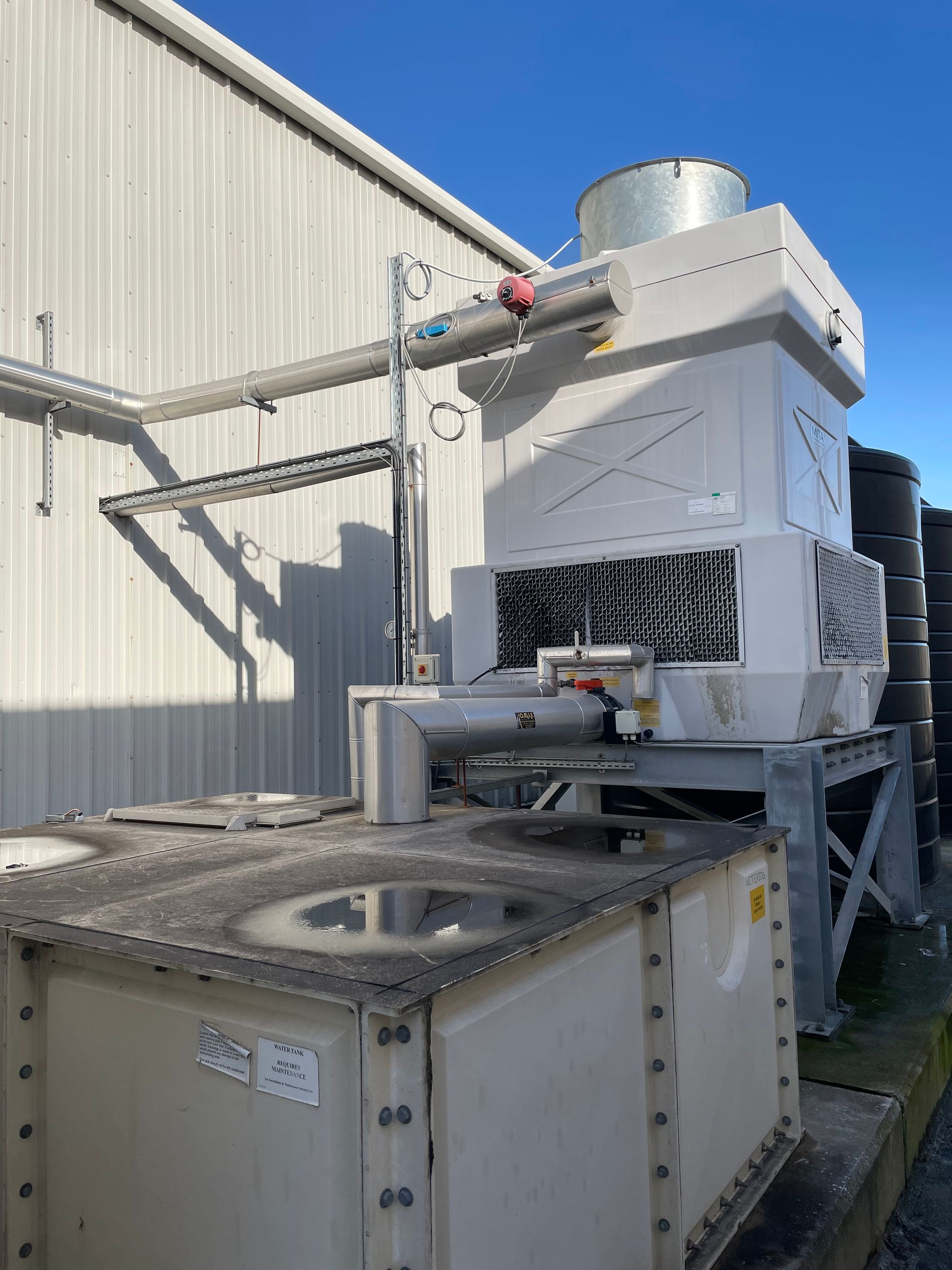White cooling tower and water tank outside industrial building under a blue sky.