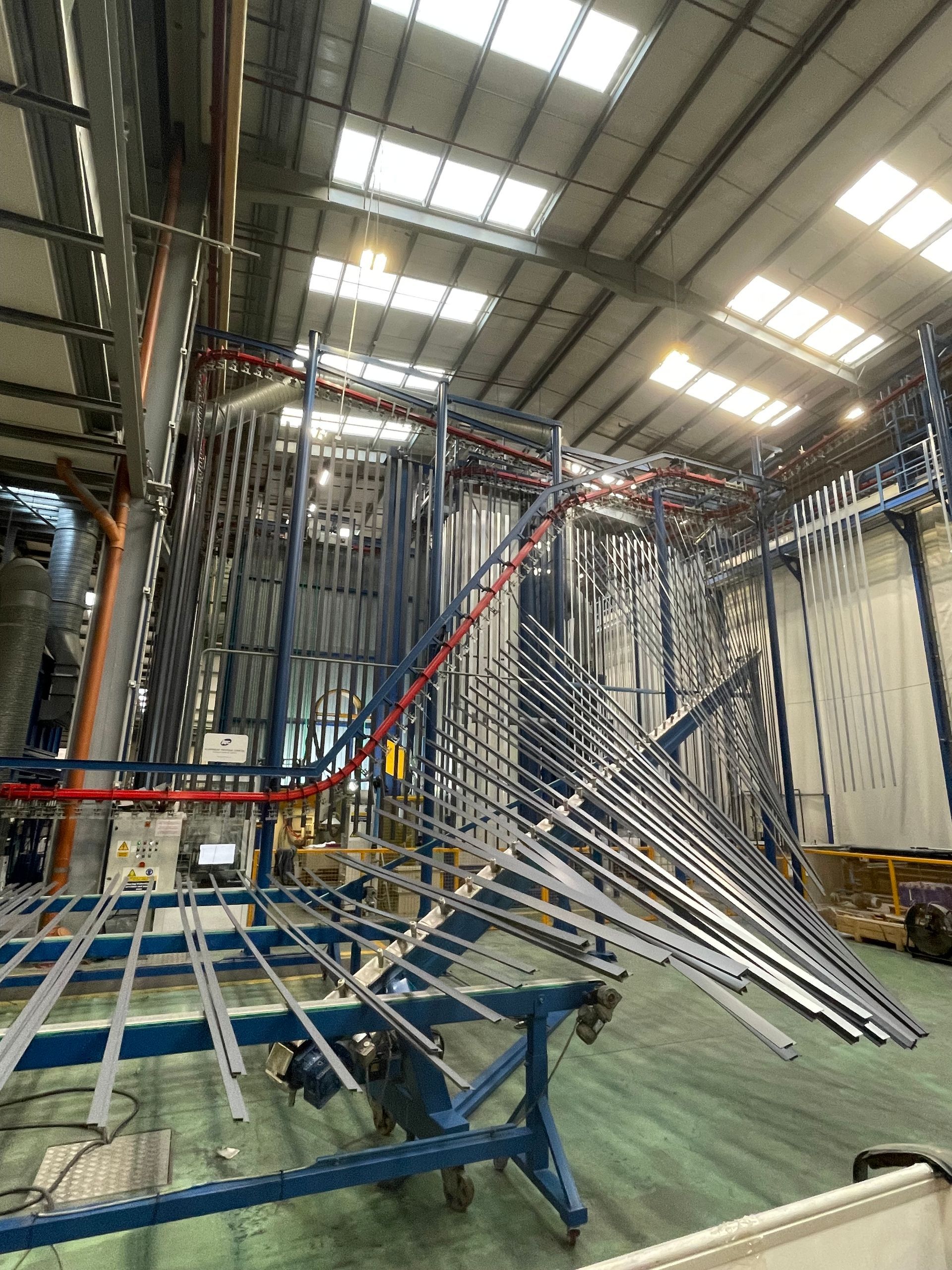 An industrial interior featuring an overhead conveyor system; metal frames hang from a track.