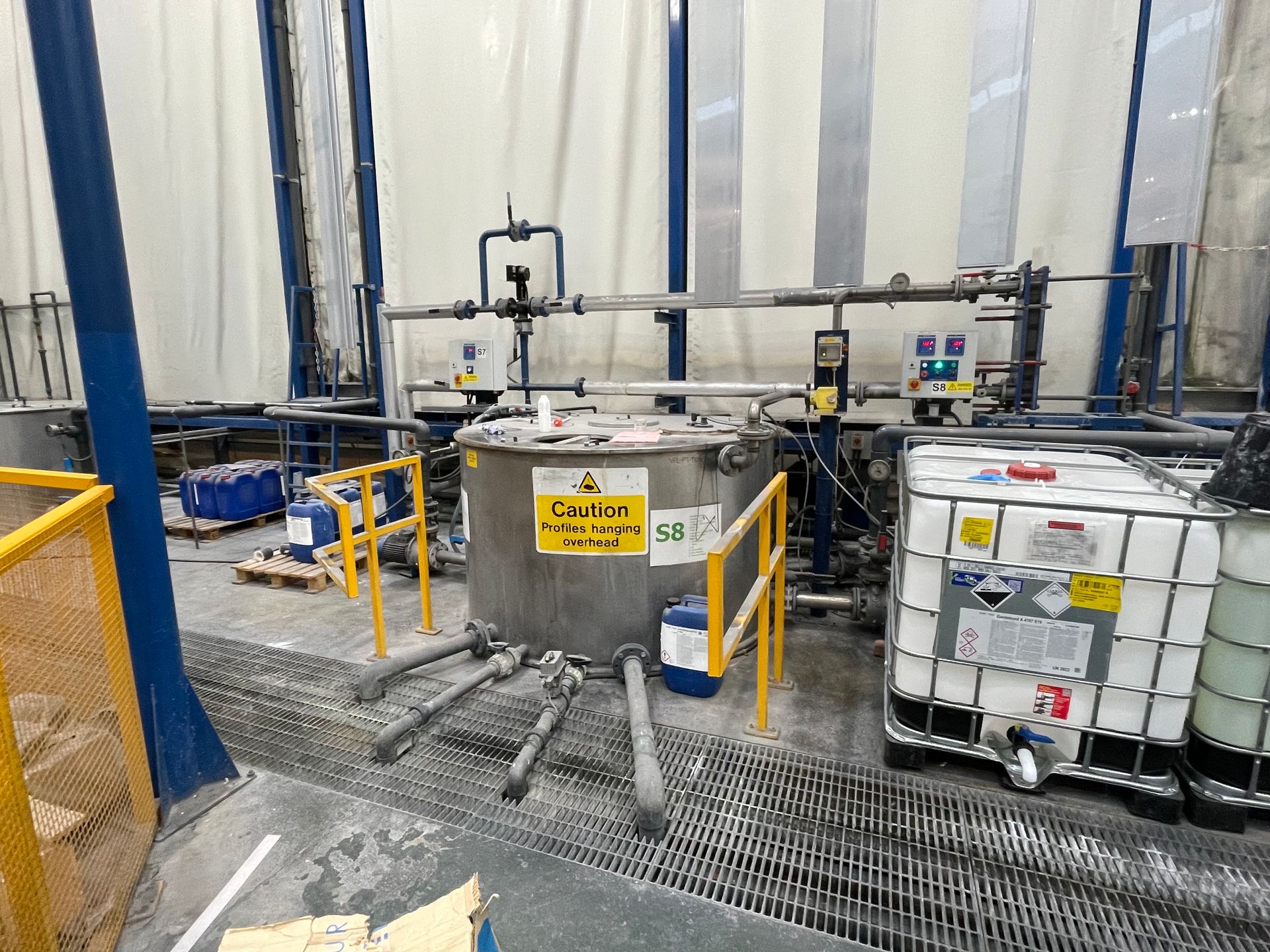 Industrial tanks and equipment in a factory setting, with warning labels and safety railings.