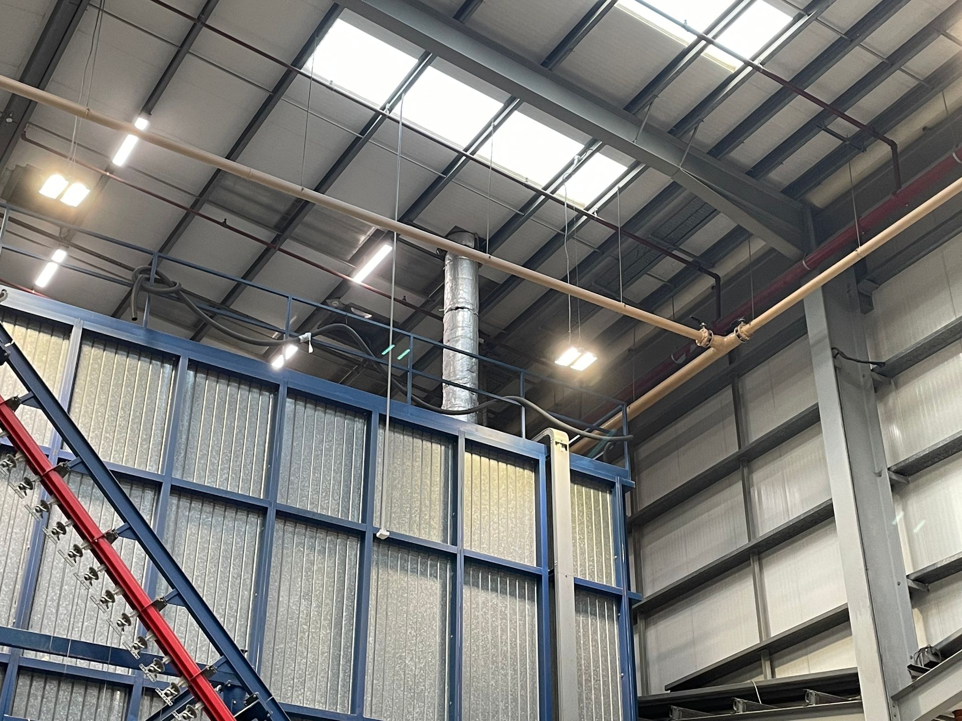 Large industrial space with blue machinery, overhead lighting, and metal beams.