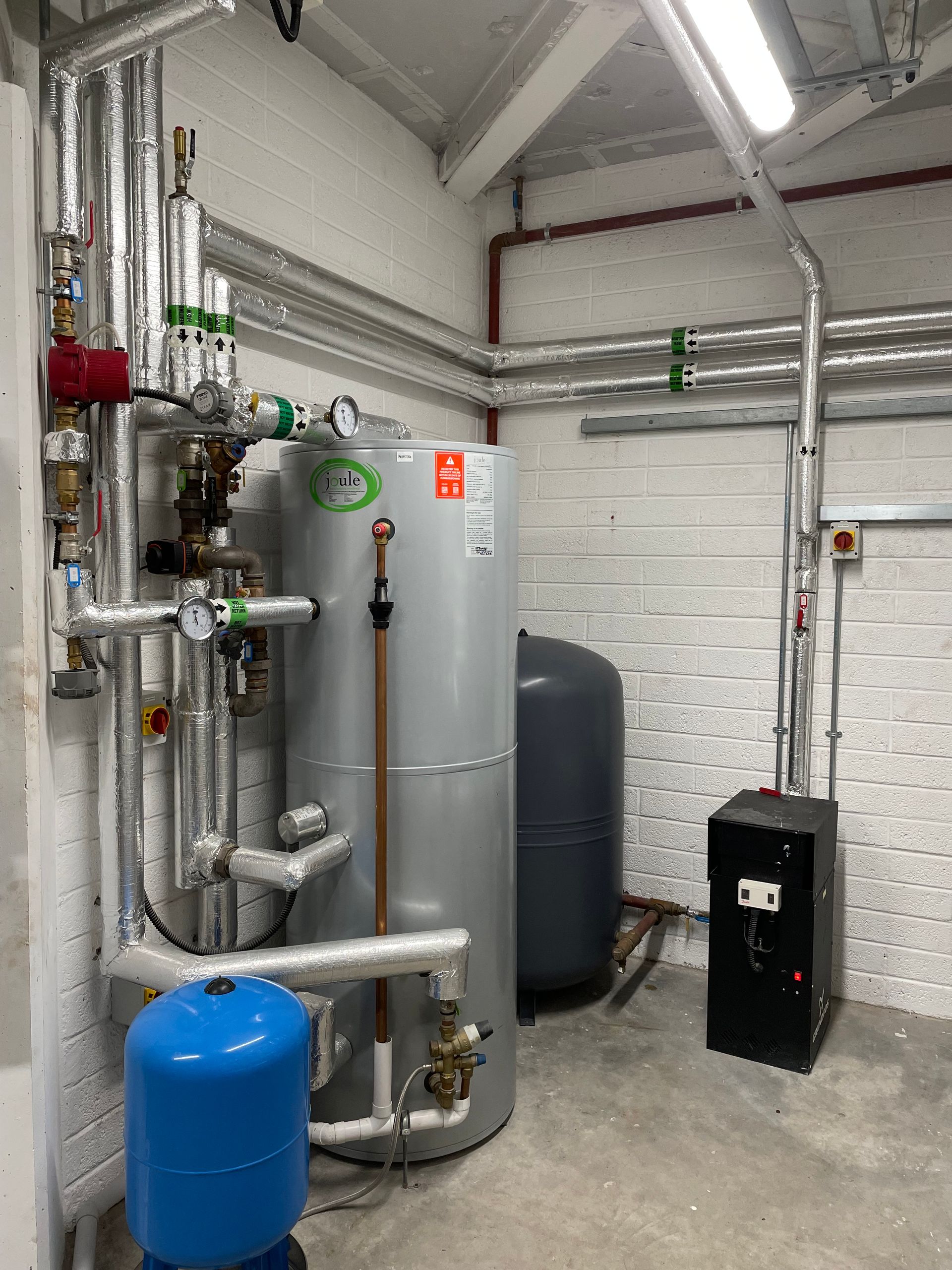 Industrial equipment: water heater, pipes, tanks, and gauges in a utility room.