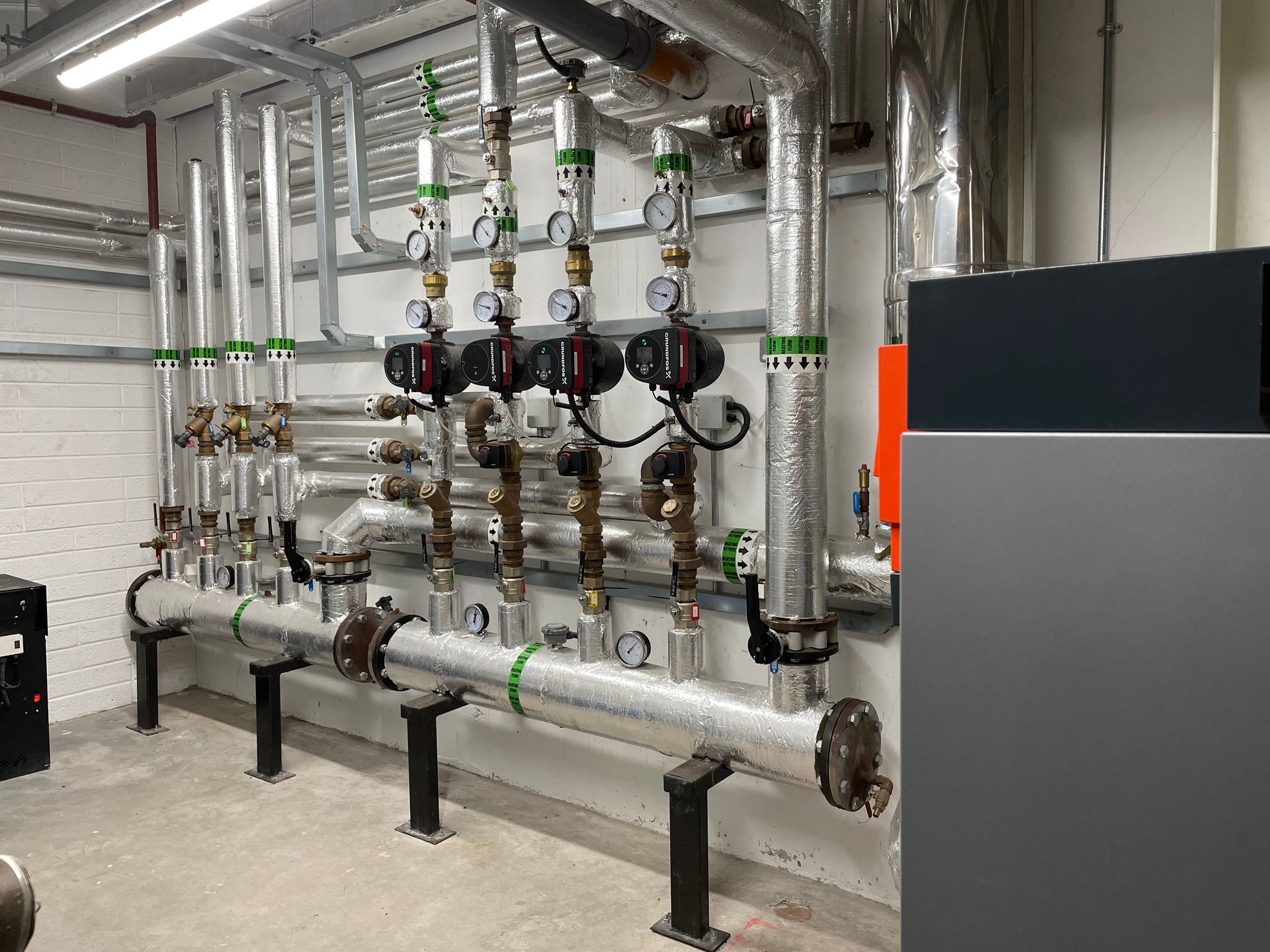 Pipes and pumps in a mechanical room, with insulation, gauges, and valves.