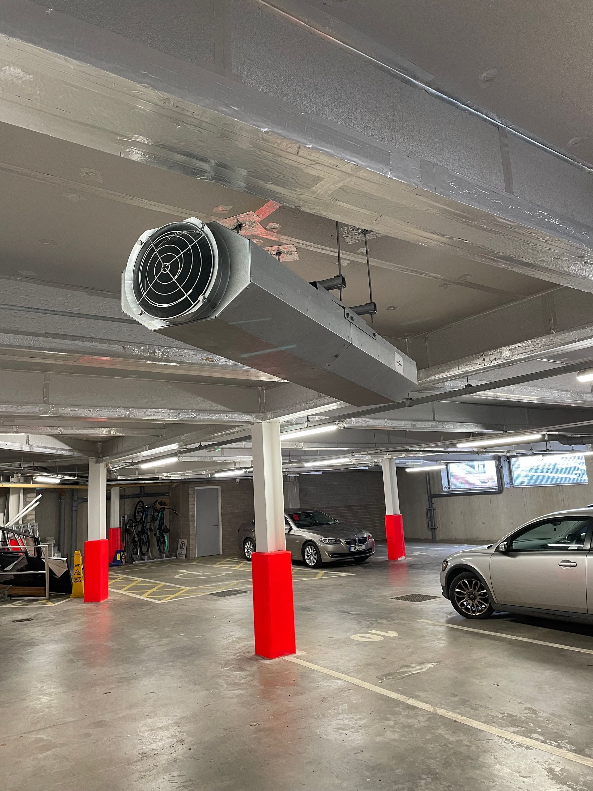 Parking garage with a long, rectangular ventilation system suspended from the ceiling. Cars are parked below.