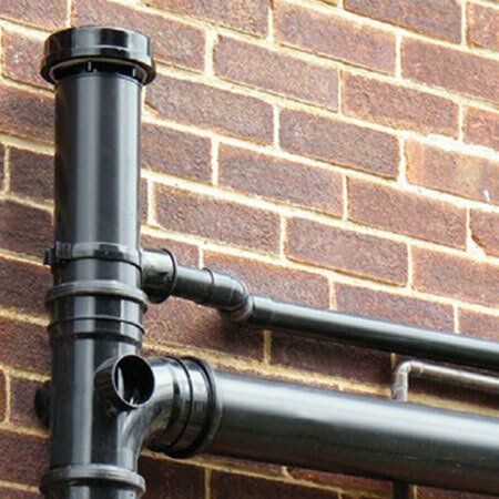 Black pipes against a brick wall, part of an external drainage system.