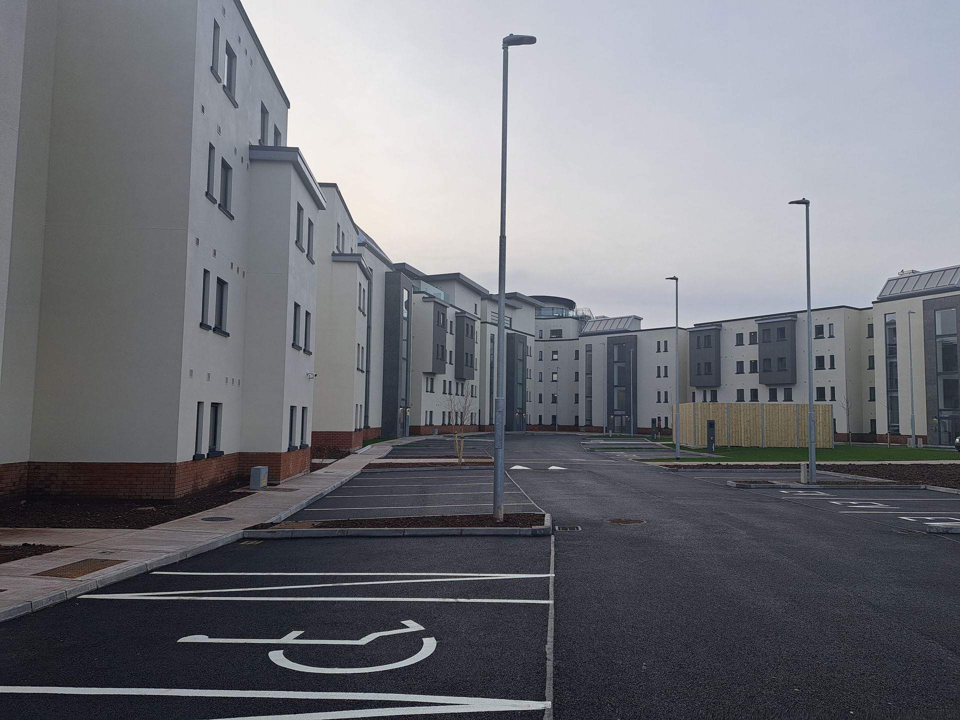 Exterior view of modern white apartment buildings, with a parking lot and lamp posts, cloudy sky.