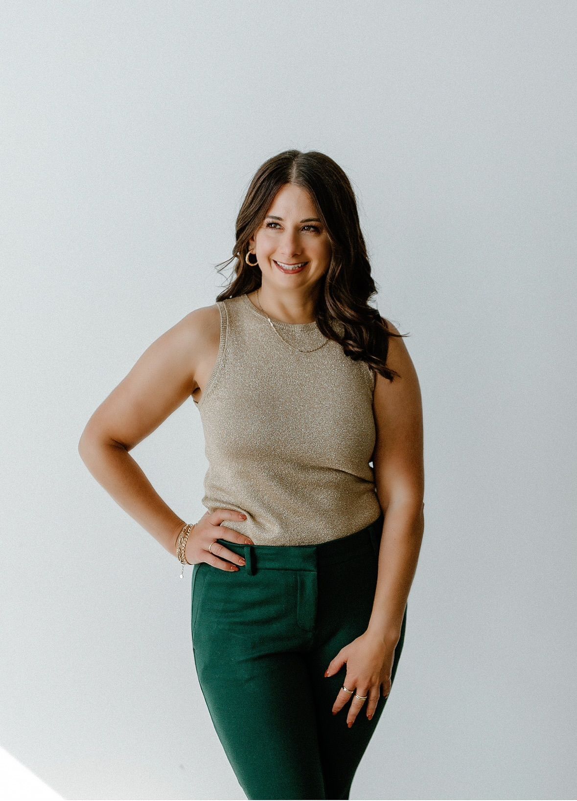Woman with dark hair, wearing a cream-colored sweatshirt and sweatpants, hands in pockets, smiling.