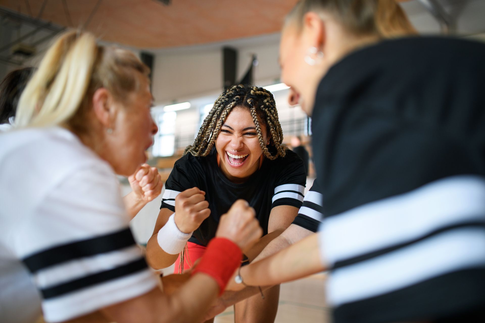 Three women cheer, celebrating together. Smiling woman in center, braids, with arms raised.