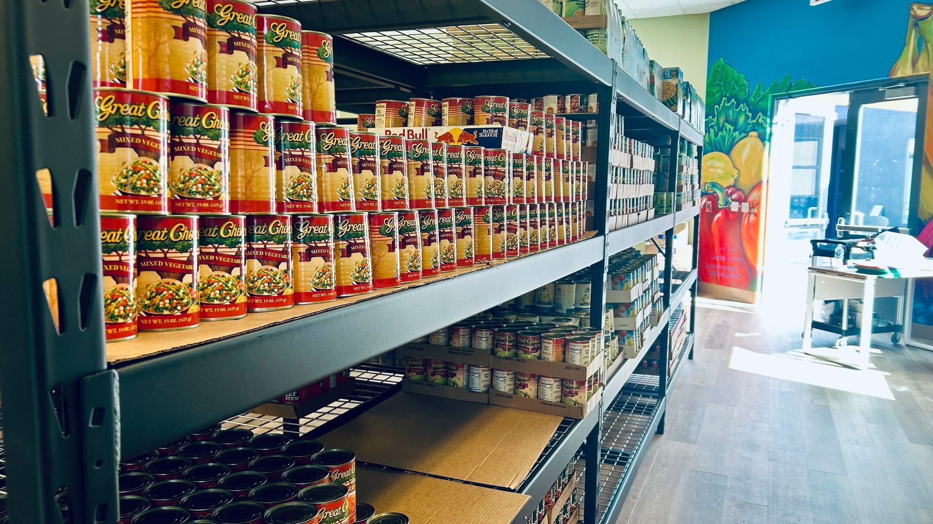 Shelves stocked with canned goods inside a room with a mural on the wall.