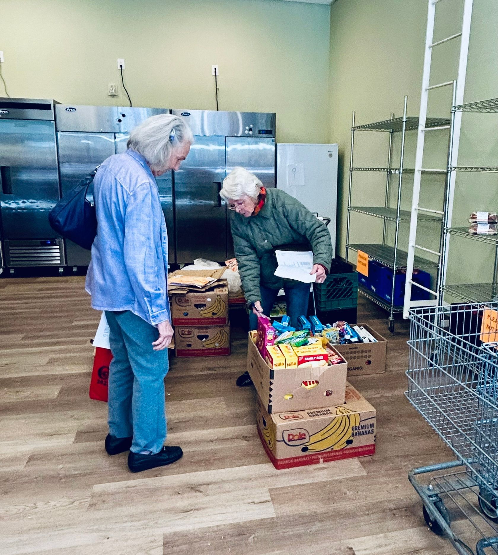 Two people in a pantry sorting food boxes. One looks at a list, the other is wearing a light blue shirt.
