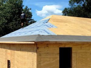 A man is standing on top of a wooden roof.