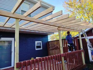 A man is standing on a deck under a wooden pergola.