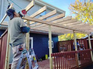 A man is standing on a ladder working on a wooden structure.