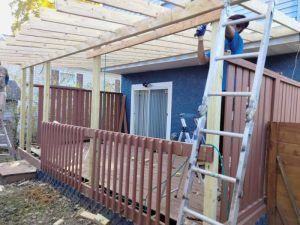 A man is standing on a ladder next to a wooden deck.