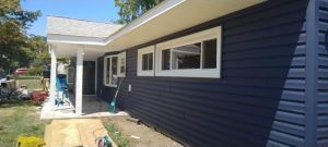 A blue house with white trim and windows is being painted.